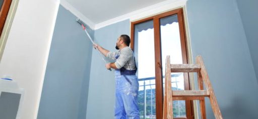 Painter man at work takes the color with paint roller from the bucket. With copy space